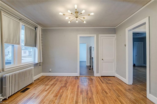 spare room with a notable chandelier, light wood-style flooring, radiator, crown molding, and baseboards