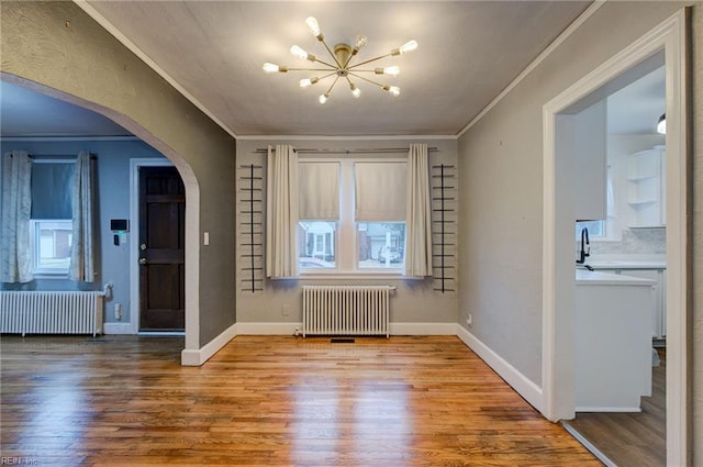 interior space featuring arched walkways, crown molding, radiator heating unit, and wood finished floors