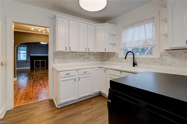 kitchen with open shelves, light wood-style flooring, arched walkways, white cabinetry, and a sink