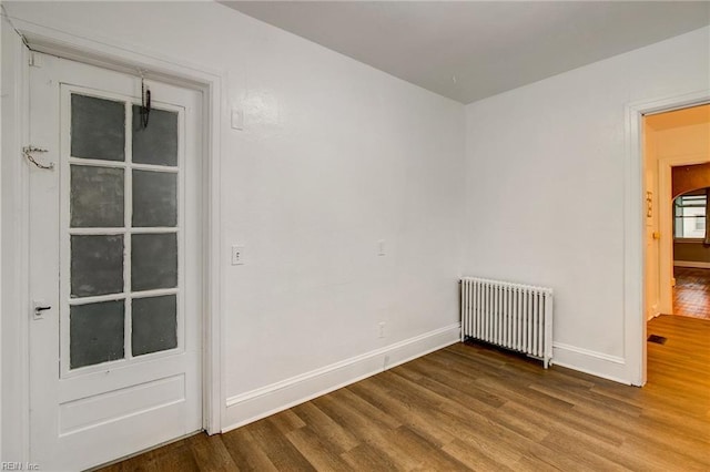 spare room with baseboards, wood finished floors, and radiator heating unit