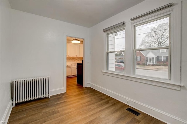 empty room with visible vents, baseboards, wood finished floors, and radiator heating unit