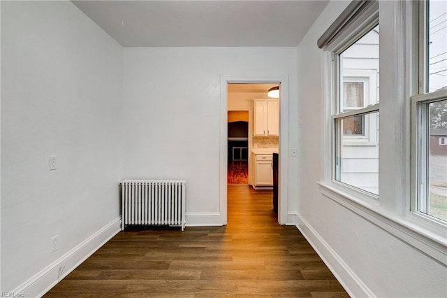 empty room with dark wood finished floors, radiator heating unit, and baseboards