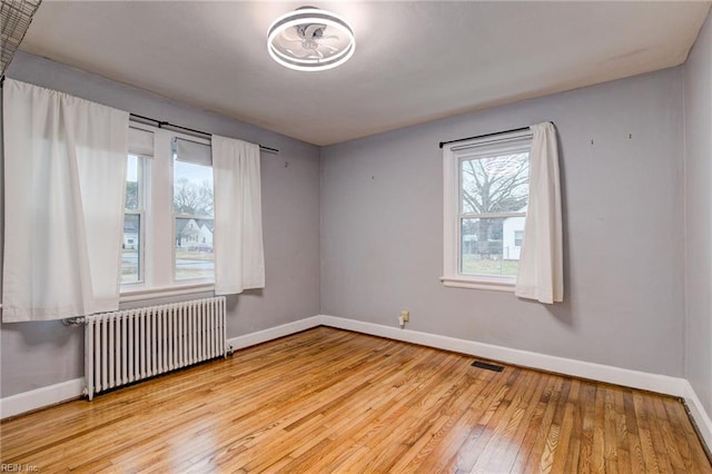 empty room featuring hardwood / wood-style floors, radiator heating unit, visible vents, and baseboards