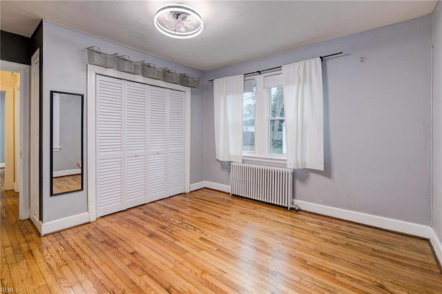 unfurnished bedroom featuring light wood-style flooring, radiator heating unit, baseboards, and a closet