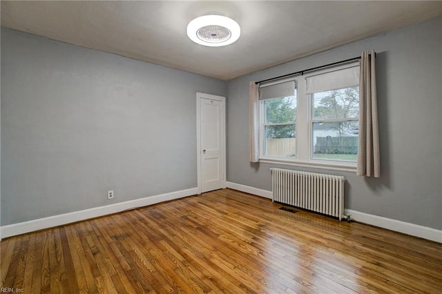 spare room featuring radiator, baseboards, and wood finished floors