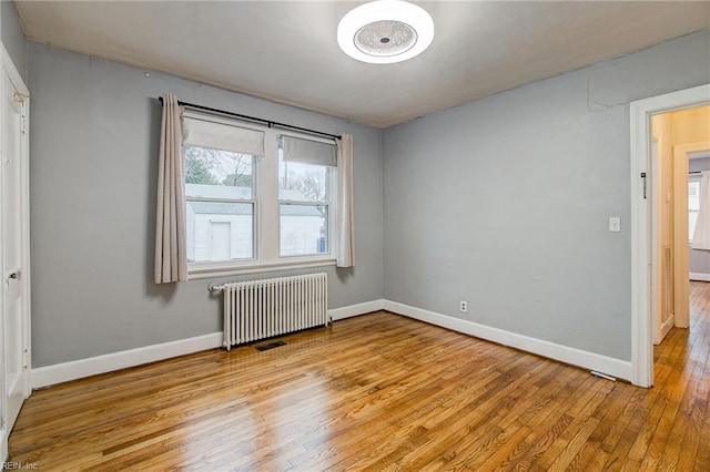 empty room featuring light wood-style flooring, radiator, and baseboards