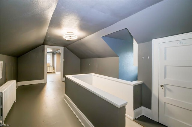 corridor with baseboards, an upstairs landing, radiator, and lofted ceiling