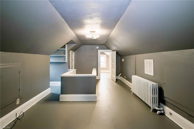 additional living space with finished concrete flooring, visible vents, baseboards, radiator heating unit, and vaulted ceiling