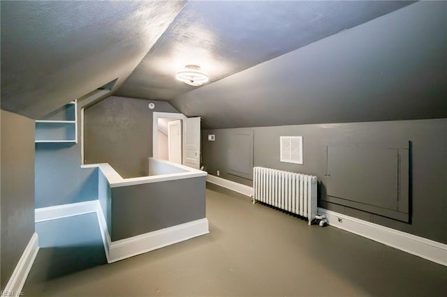 additional living space with baseboards, concrete floors, radiator heating unit, and vaulted ceiling