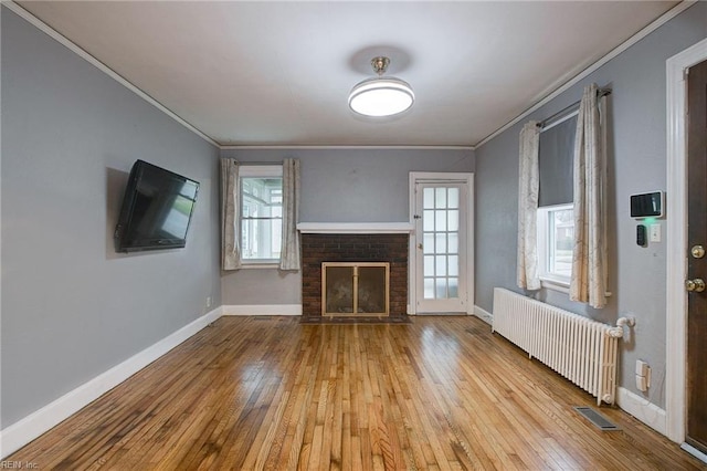 unfurnished living room featuring radiator, a brick fireplace, hardwood / wood-style floors, and crown molding