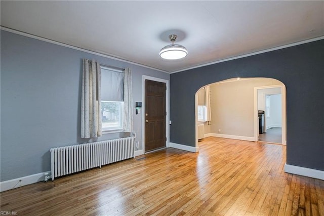 foyer entrance featuring radiator, baseboards, light wood-style flooring, arched walkways, and crown molding