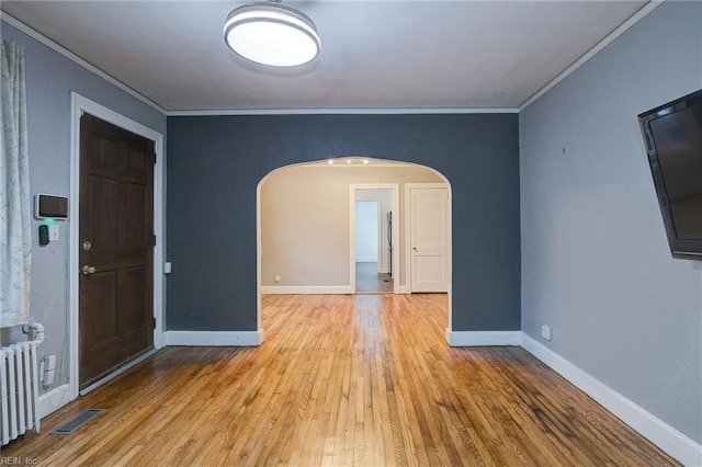 empty room featuring radiator, baseboards, arched walkways, ornamental molding, and hardwood / wood-style flooring