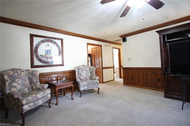 sitting room with ceiling fan, a wainscoted wall, ornamental molding, and carpet flooring