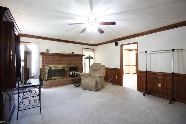 carpeted living area featuring a ceiling fan, crown molding, a fireplace, and wainscoting