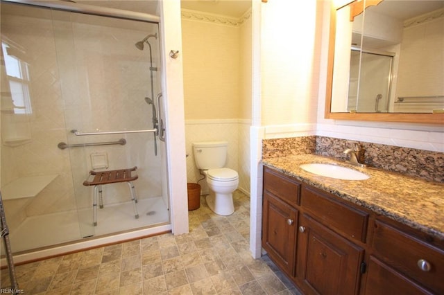 full bath with a wainscoted wall, toilet, tile walls, a shower stall, and vanity