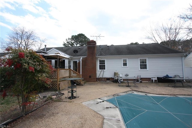 back of house with a covered pool, a patio, crawl space, and a chimney