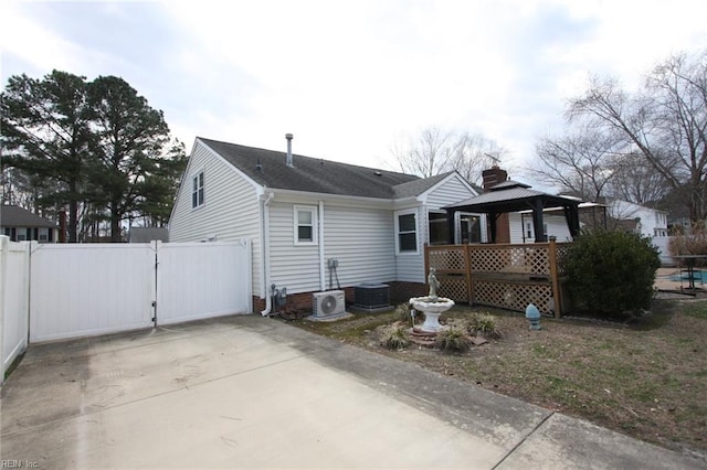 back of house featuring driveway, a gate, fence, a gazebo, and a chimney