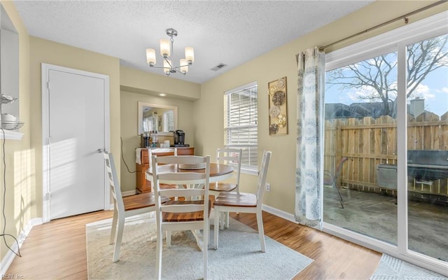 dining space with a wealth of natural light, visible vents, light wood-type flooring, and an inviting chandelier