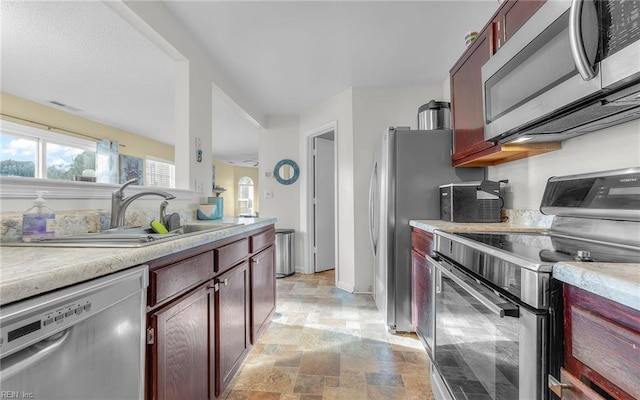 kitchen featuring dark brown cabinets, light countertops, appliances with stainless steel finishes, stone finish floor, and a sink