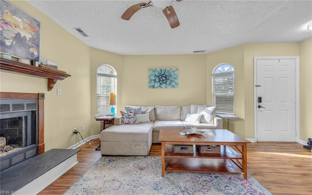 living room featuring visible vents, wood finished floors, baseboards, and a fireplace with raised hearth