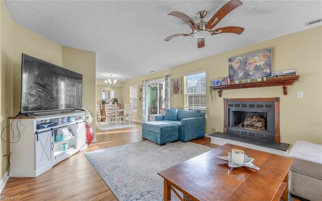 living room with a ceiling fan, wood finished floors, visible vents, a fireplace with raised hearth, and a textured ceiling