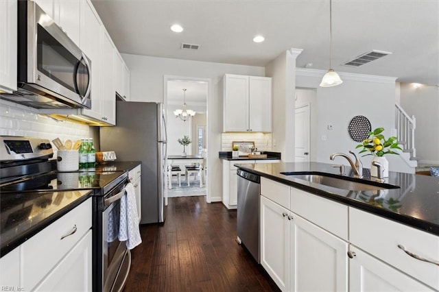 kitchen with visible vents, a sink, hanging light fixtures, stainless steel appliances, and dark countertops