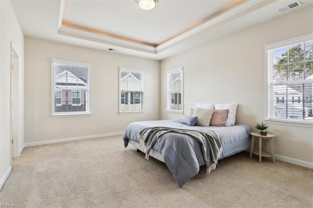 bedroom with a tray ceiling, multiple windows, visible vents, and light carpet