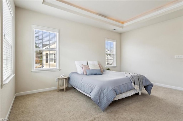 bedroom with baseboards, multiple windows, a raised ceiling, and light carpet