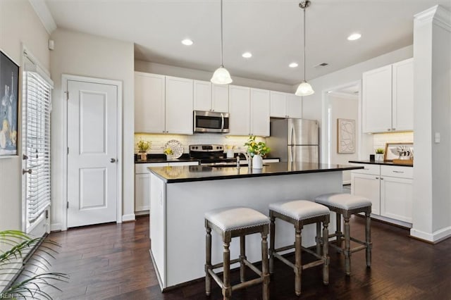 kitchen featuring dark countertops, a kitchen breakfast bar, dark wood-style floors, white cabinets, and stainless steel appliances