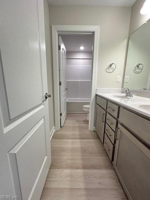 bathroom with wood finished floors, double vanity, a sink, shower / tub combination, and toilet