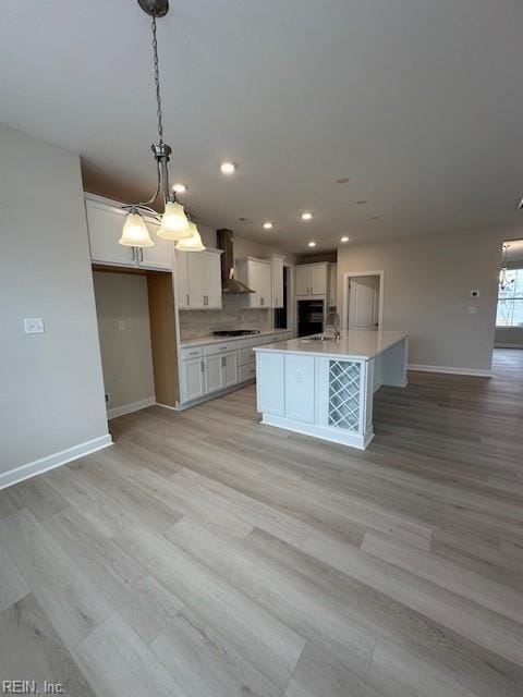 kitchen featuring white cabinetry, light countertops, wall chimney range hood, and baseboards