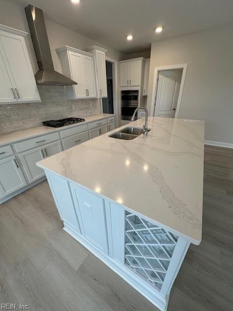 kitchen featuring a sink, gas cooktop, tasteful backsplash, wall chimney exhaust hood, and white cabinets