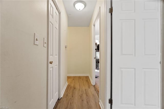 corridor with light wood-type flooring and baseboards