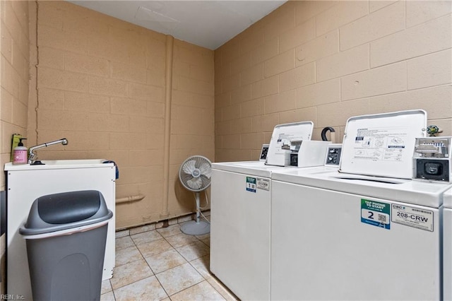 shared laundry area featuring concrete block wall, light tile patterned floors, and washer and clothes dryer