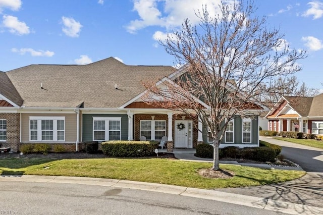 view of front of home with brick siding, roof with shingles, and a front lawn