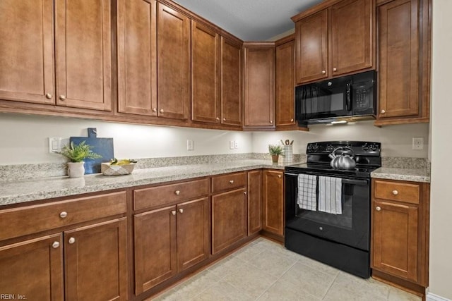 kitchen featuring light tile patterned floors, brown cabinets, black appliances, and light stone countertops