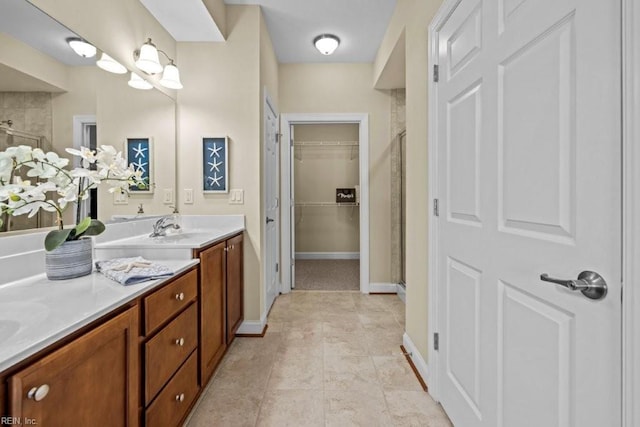 full bath with a walk in closet, a sink, a shower stall, double vanity, and baseboards