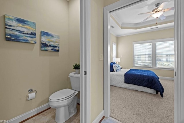 ensuite bathroom featuring crown molding, toilet, a raised ceiling, and baseboards