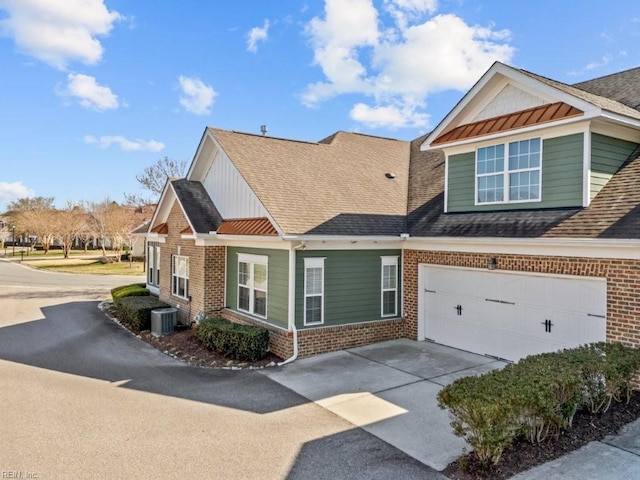 view of front facade featuring central AC, concrete driveway, an attached garage, a shingled roof, and brick siding