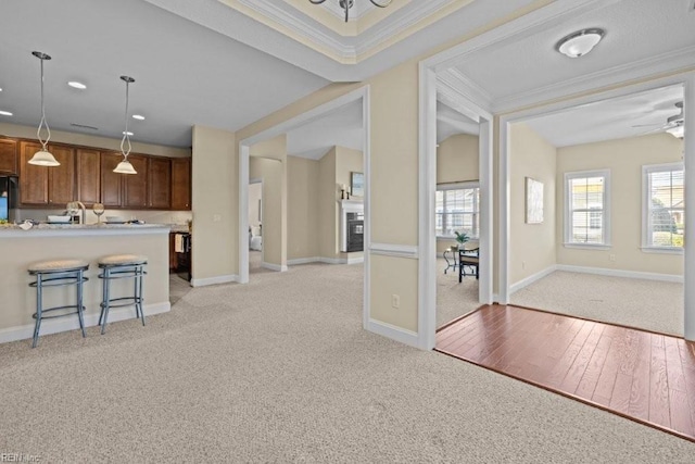 interior space with a breakfast bar area, brown cabinetry, crown molding, baseboards, and hanging light fixtures