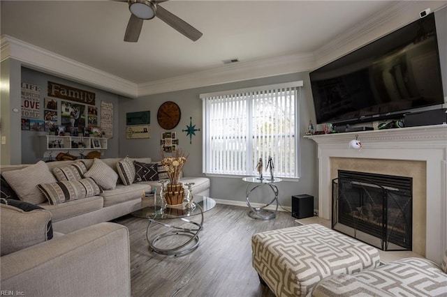 living room featuring visible vents, crown molding, wood finished floors, a glass covered fireplace, and a ceiling fan