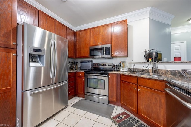 kitchen with crown molding, light tile patterned floors, dark stone countertops, appliances with stainless steel finishes, and a sink