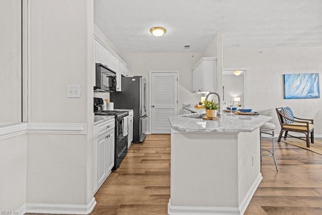 kitchen with black appliances, a kitchen breakfast bar, light wood finished floors, and white cabinets