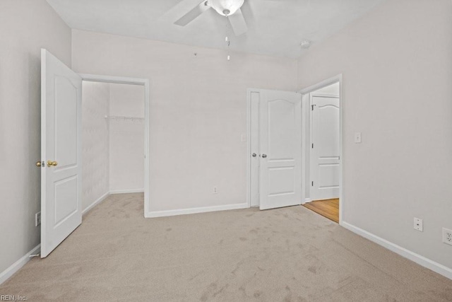 unfurnished bedroom with carpet flooring, ceiling fan, a walk in closet, and baseboards