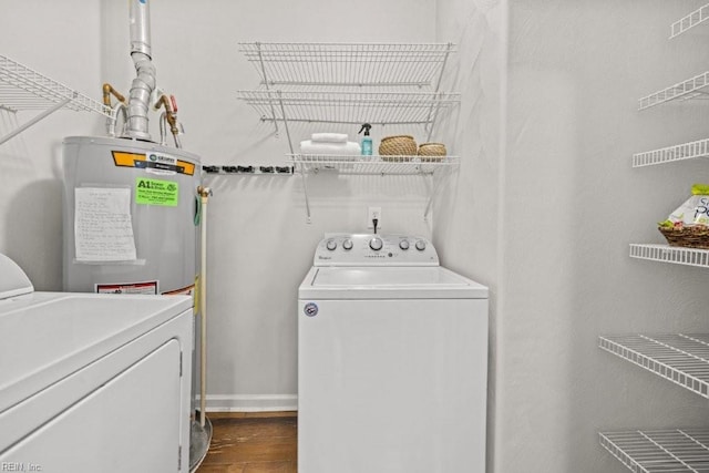 clothes washing area with dark wood-style flooring, washing machine and dryer, laundry area, and electric water heater