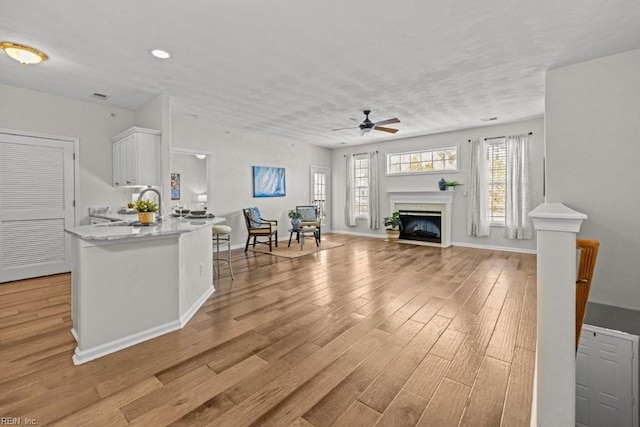 kitchen with light wood-style flooring, a peninsula, white cabinets, a fireplace, and ceiling fan