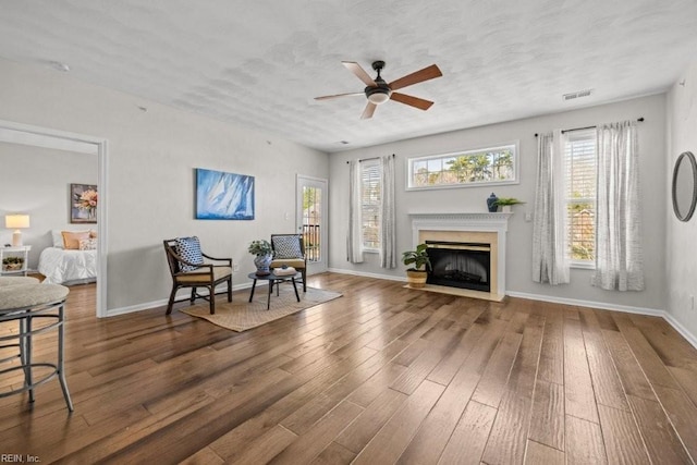 living area featuring hardwood / wood-style floors, a ceiling fan, visible vents, baseboards, and a fireplace with flush hearth