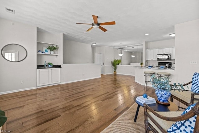 living area with visible vents, wood finished floors, baseboards, and ceiling fan