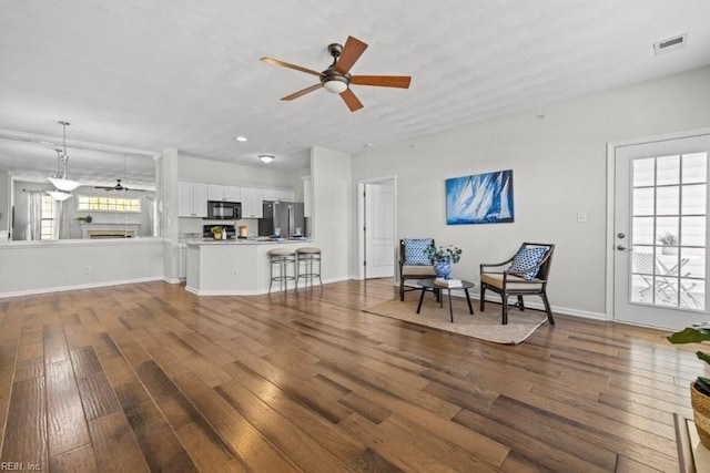 living area with visible vents, baseboards, a ceiling fan, and hardwood / wood-style flooring