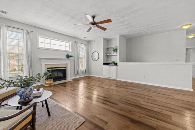 living room with built in shelves, a textured ceiling, wood finished floors, a high end fireplace, and ceiling fan